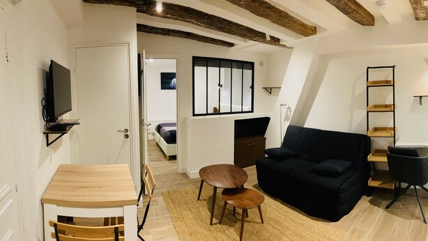 Un salon moderne avec un canapé noir, une table basse en bois et un téléviseur. Un escalier mène à un niveau supérieur.