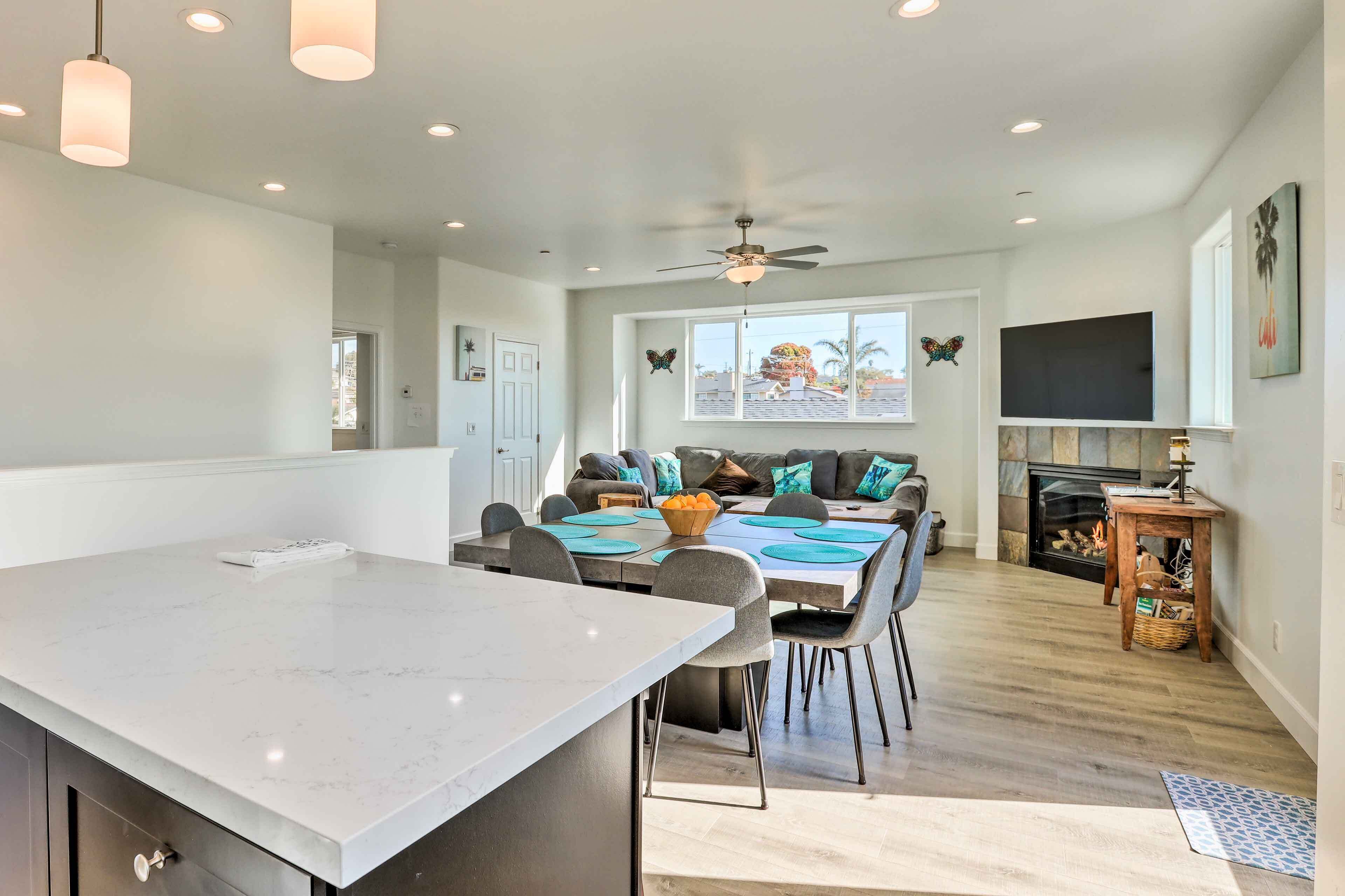A spacious kitchen with a large island, dining area with chairs and a table, a fireplace, and a ceiling fan.