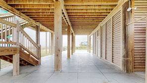 A covered wooden structure with a concrete floor, wooden railings, and a view of a house in the distance.