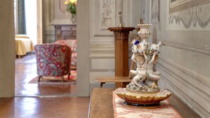 Un couloir agrémenté d’une fontaine décorative, d’un fauteuil à motifs et d’une table sur laquelle est posé un vase de fleurs.
