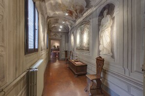 Ein langer, schmaler Korridor mit aufwendigen Zierarbeiten an der Decke, einem Heizkörper links und einer hölzernen Bank rechts.
