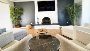 A modern living room with a fireplace, two sofas, a coffee table, and potted plants. - Lake house with hot tub, pool, game room & BBQ grill (Lake Elsinore)