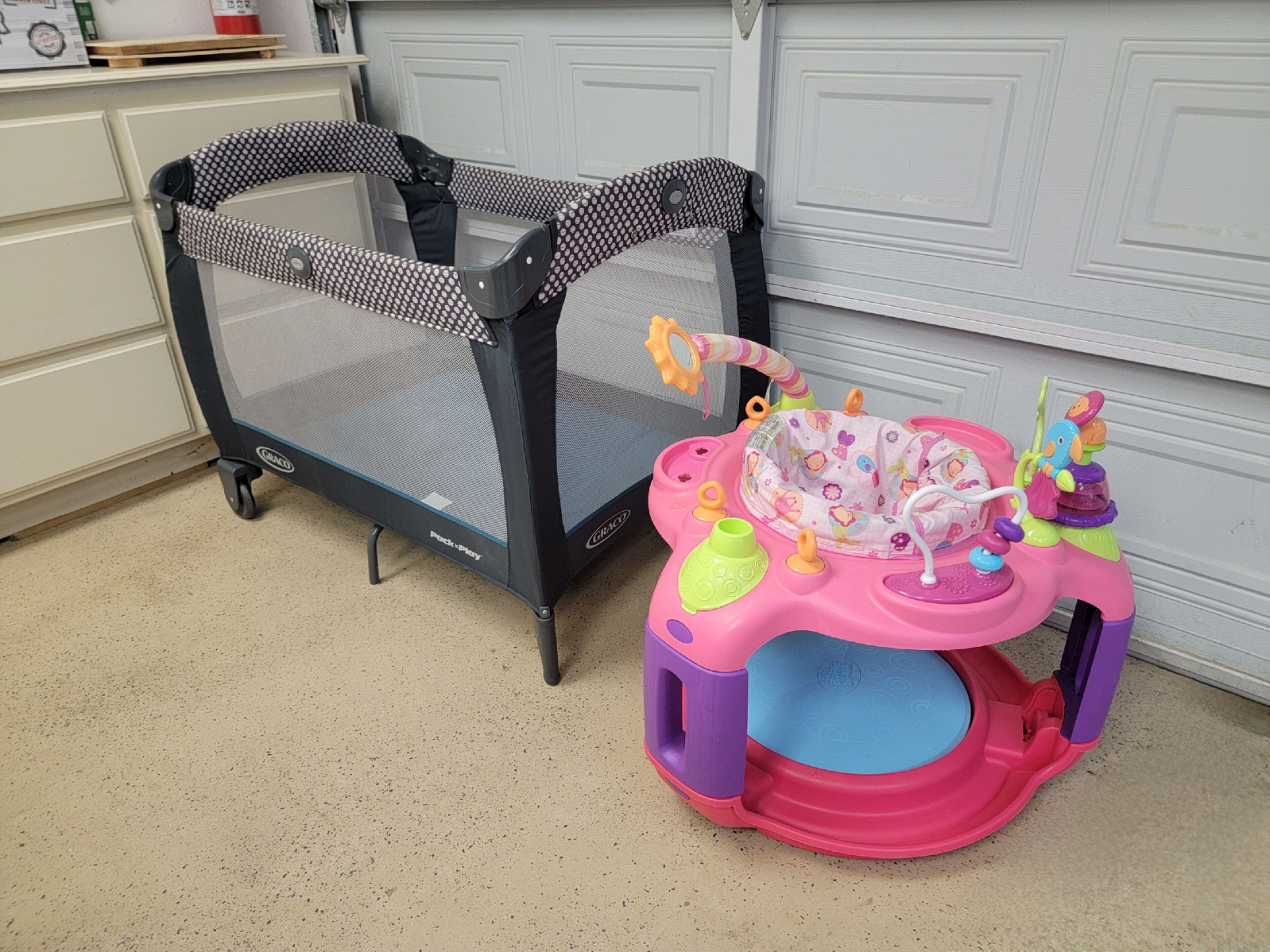 A playpen with a mesh top and a colorful play table with toys.