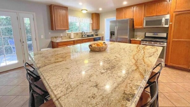 A kitchen with granite countertops, wooden cabinets, stainless steel appliances, and a large island with a fruit bowl. - Lake house with hot tub, pool, game room & BBQ grill (Lake Elsinore)