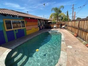 A swimming pool with clear water, surrounded by a wooden fence and a colorful building with a tiled roof.