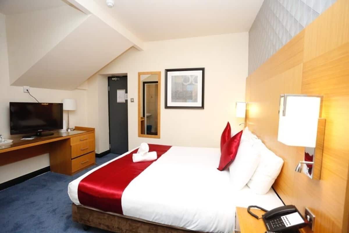 Une chambre d’hôtel avec un lit, un bureau avec une télévision, un téléphone et un miroir au mur.