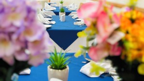 A table set with white napkins and a blue tablecloth, surrounded by potted plants and flowers. - Acorn Lodge Gatwick (Horley)