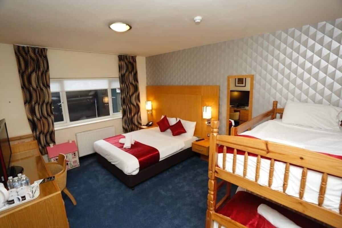 Une chambre d’hôtel avec un grand lit, un plus petit lit, un bureau avec une chaise, une télévision et une fenêtre avec des rideaux.