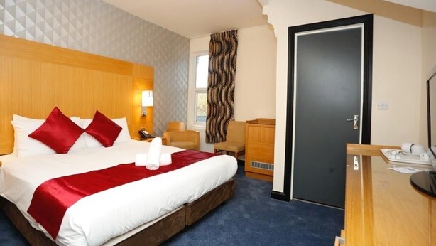 A hotel room with a large bed, a wooden headboard, a desk with a chair, and a door. - Acorn Lodge Gatwick (Horley)