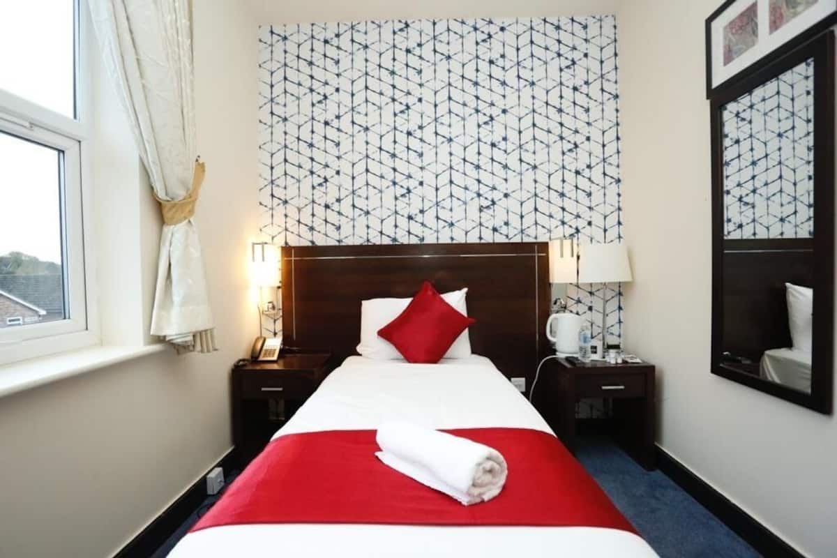 Une chambre d’hôtel avec un grand lit, une tête de lit, une table de chevet, une lampe, un miroir et une fenêtre avec des rideaux.