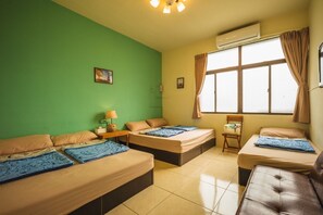 Habitación con dos camas, una mesita pequeña y una silla. Se ve una ventana con cortinas, un equipo de aire acondicionado y un cuadro en la pared.