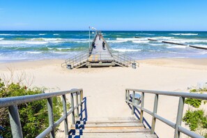 A wooden pier leading to a small structure with railings, overlooking a beach with waves. - Apartment with a playground, close to the beach (Sarbinowo)