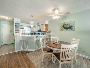 A kitchen with a central island, bar stools, a dining table with chairs, and a ceiling fan.