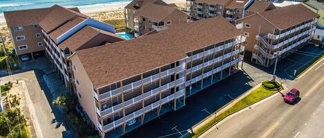 A multi-story hotel with a parking lot, located near a beach with ocean views.
