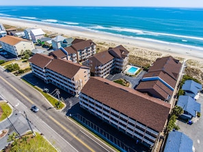 A coastal hotel with multiple buildings, a parking lot, and a beach view.