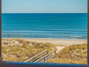 A beach with a wooden boardwalk leading to the water, sandy dunes, and a clear view of the ocean.