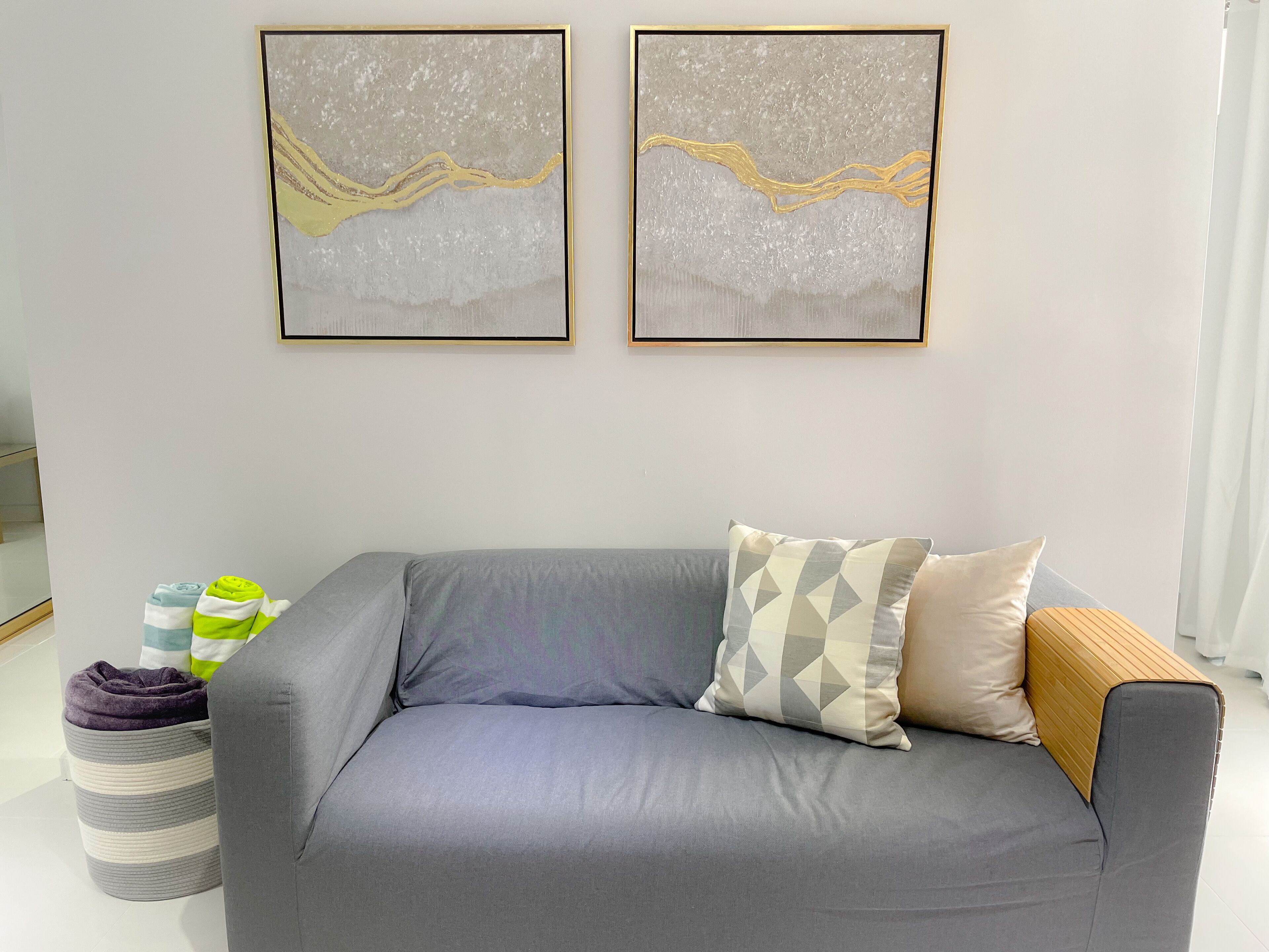 Un salon moderne avec un canapé gris, deux tableaux abstraits encadrés et un pouf rayé.