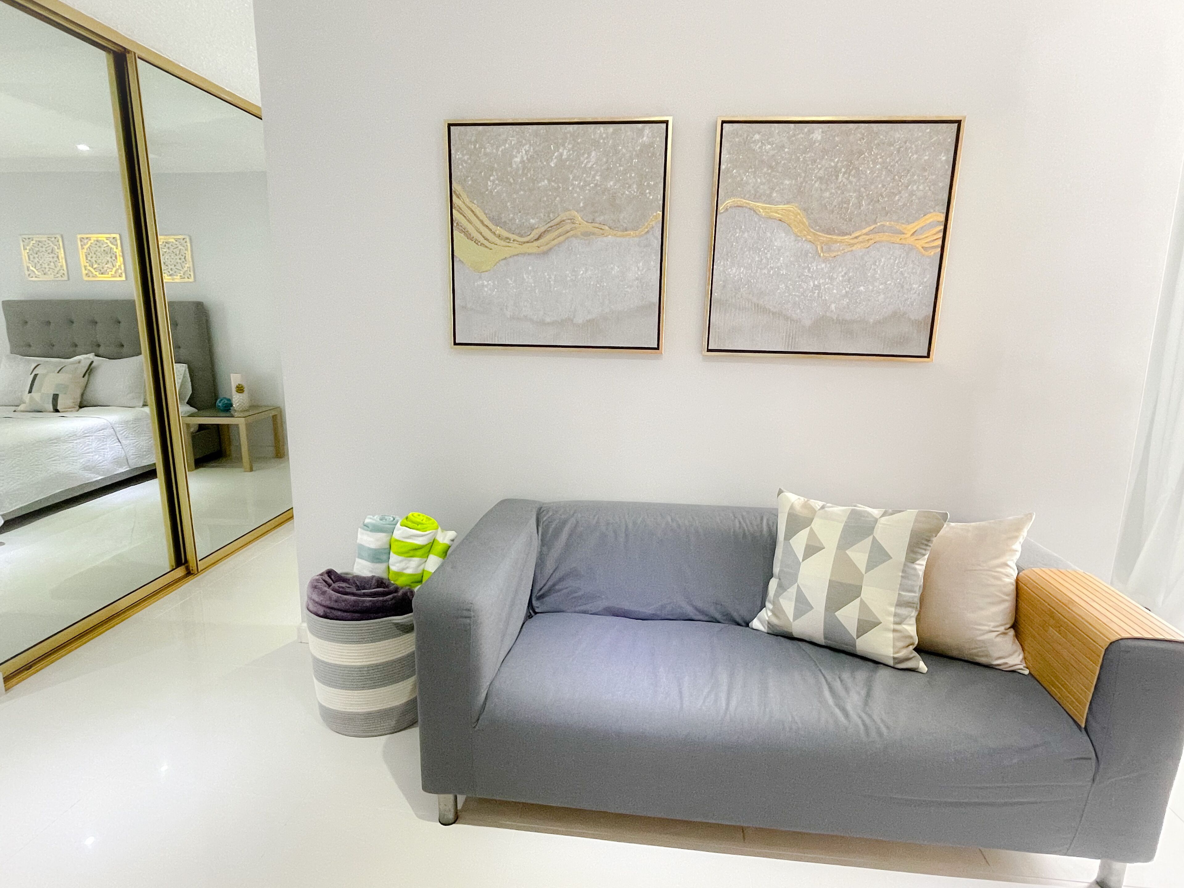 A modern living room with a grey sofa, a striped ottoman, and two abstract paintings on the wall.