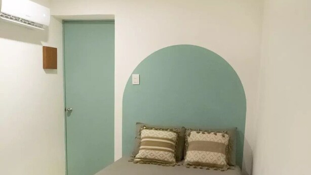 A small, single-bed room with a teal arch over the bed, a wooden bench in the foreground, and a white door. - Shalom, The peace you need when traveling. (Campeche)