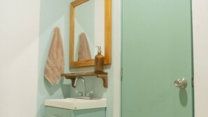 A bathroom with a light blue wall, a wooden-framed mirror, a white sink, and a door with a round handle. - Shalom, The peace you need when traveling. (Campeche)