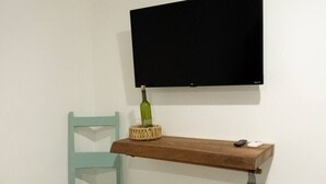 A room with a teal chair, a wooden shelf, a television, and a small basket. - Shalom, The peace you need when traveling. (Campeche)