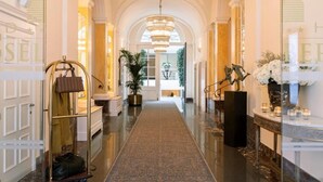 Un hall d’hôtel luxueux, avec un sol en marbre, un lustre central et une vue sur la salle à manger.