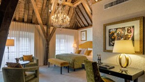 Une chambre d’hôtel avec un plafond en bois, un lustre, un lit avec une literie verte, un bureau avec une lampe et un tableau au mur.