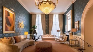 Un salon spacieux agrémenté d’un grand lustre, d’un canapé, d’un pouf rond et d’une table basse.