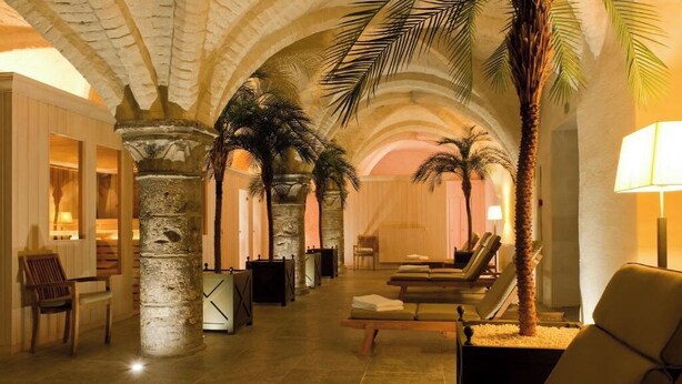 Un hall d’hôtel avec des colonnes en pierre, des palmiers et des fauteuils.