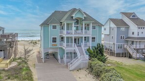 A beachfront property with a two-story house featuring a balcony, a staircase leading to the upper floor, and a view of the ocean. - Premier Oceanfront Home w/ Pool, Elevator, Hot Tub, Theater Room (Avon)