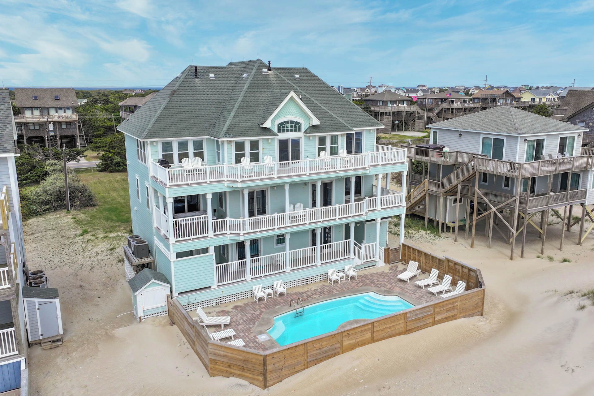 Ein mehrstöckiges Strandhaus mit Swimmingpool, Balkonen und einer Holzterrasse.