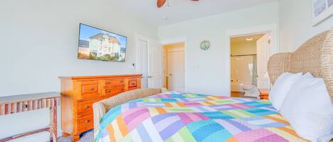 Een slaapkamer met een groot bed, een houten dressoir, een plafondventilator, een televisie en een badkamer die door een open deur zichtbaar is.