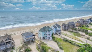 A beachfront property with multiple houses, some elevated on stilts, and a sandy beach in the background. - Premier Oceanfront Home w/ Pool, Elevator, Hot Tub, Theater Room (Avon)