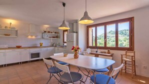 Una cocina moderna con armarios blancos, una isla central y un comedor con sillas azules.