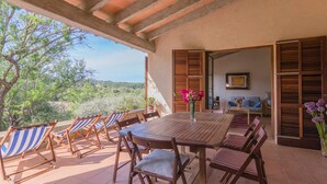 Un patio con mesa y sillas de madera, un florero con flores y vistas al paisaje.