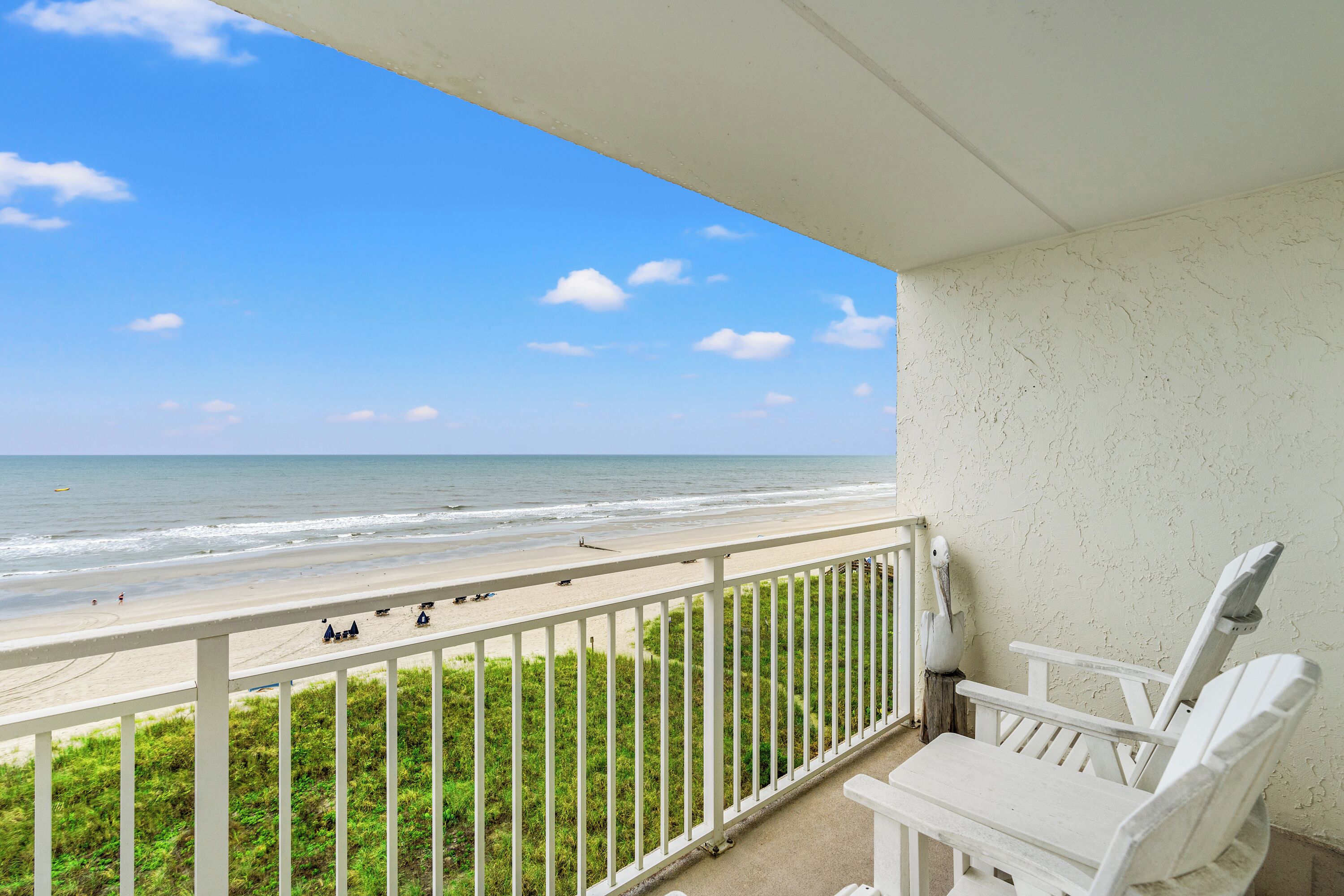 Un balcón con vista a la playa, una silla blanca y una barandilla blanca.