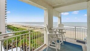 A balcony with white chairs and a table, overlooking a beach with people and a pool. - Views & Indoor Pool - San A Bel 315 (North Myrtle Beach)