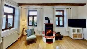 A living room with a wooden floor, a central fireplace, a sofa, a TV, and windows with curtains. - Vacation home Wolthuser Warf 3 - emden and sea - idyllic living for 4 close to the city (Emden)