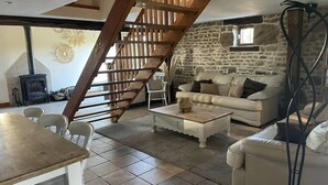 Una sala de estar acogedora con pared de piedra, escalera de madera, chimenea y un sofá.