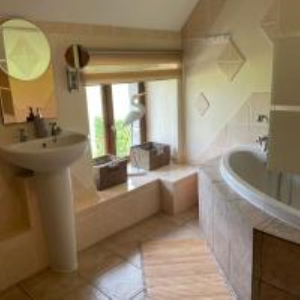 Une salle de bain avec un lavabo sur colonne, une baignoire et une fenêtre laissant entrer la lumière naturelle.