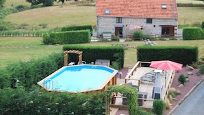 Una casa de piedra con techo rojo, piscina y terraza amueblada al aire libre.
