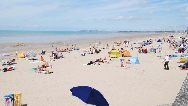 Una playa concurrida con gente tomando el sol, tiendas de campaña y sombrillas.