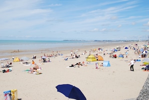 A crowded beach with people sunbathing, tents, and umbrellas.
