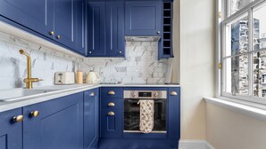 A kitchen with blue cabinets, a white countertop, a built-in oven, and a window with a city view.