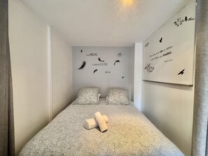 A bedroom with a patterned bedspread, two pillows, a wall with feather decorations and a quote, and a framed quote on the wall. - Jolies Lavandes (Cannes)