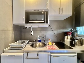 A compact kitchen with a built-in microwave, a sink, and a compact refrigerator. - Jolies Lavandes (Cannes)