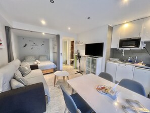 A compact hotel room with a bed, a dining table, a TV, and a kitchenette. - Jolies Lavandes (Cannes)
