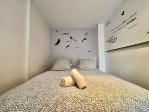 A bedroom with a patterned bedspread, two pillows, and a wall with a quote.
