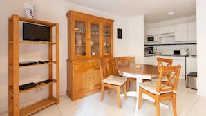 Eine kleine Küche mit Esstisch und Stühlen, einem Holzschrank mit Glastüren und einem Fernseher auf einem Regal.