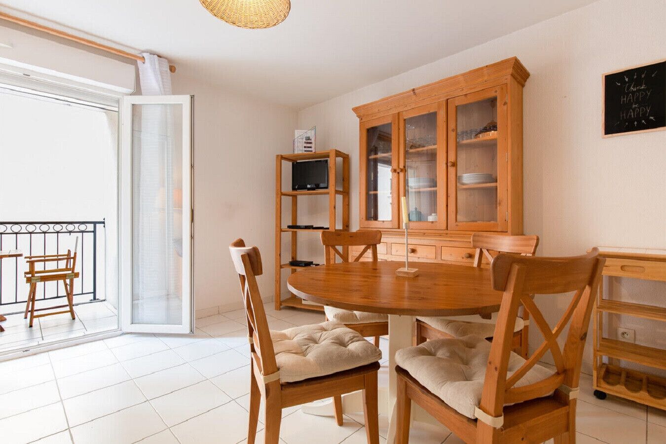 A dining area with a round wooden table, cushioned chairs, a wooden cabinet with glass doors, and a sliding glass door leading to a balcony.